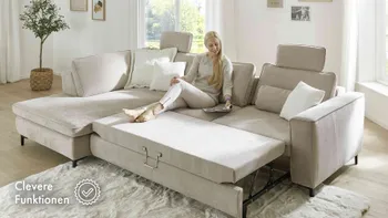 Frau sitzt auf einem zum Bett umfunktioniertem Sofa und liest ein Möbelmagazin